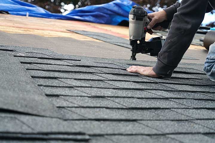 handyman using nail gun to install shingle to repair roof