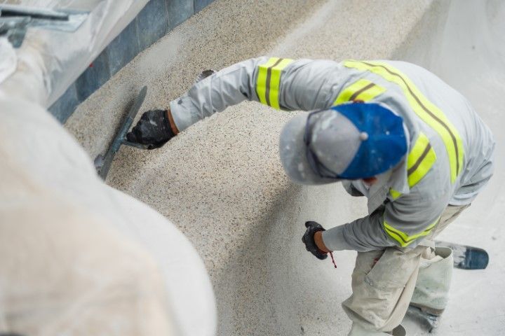 Worker in reflective vest and blue helmet shovels gravel in a construction site.