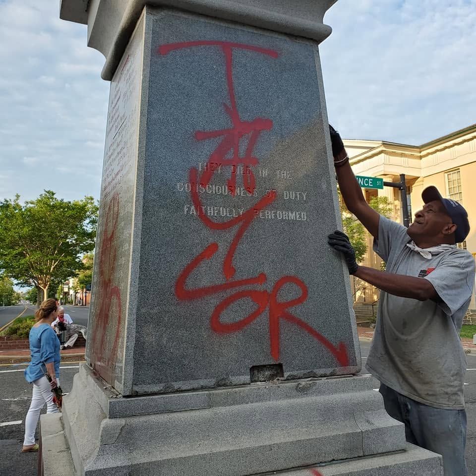 Person spray-painting red graffiti on a stone monument base outdoors