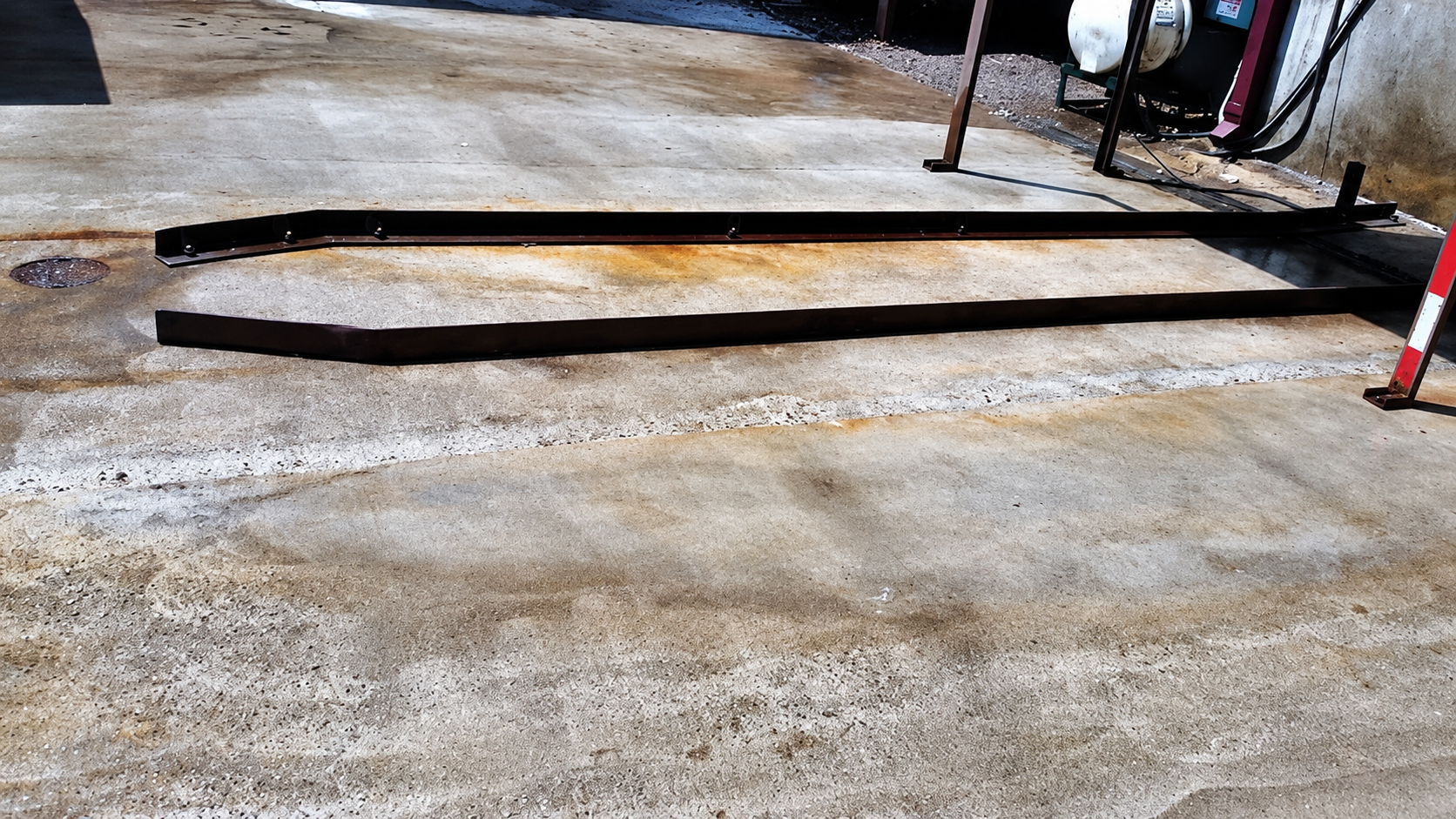 Long black metal beams lying on gravel in an outdoor work area