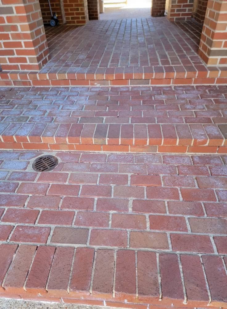 Brick walkway with steps and a small drain grate leading to a covered entrance