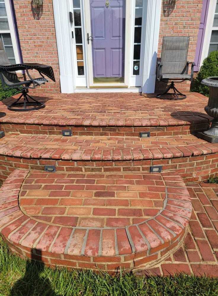 Brick front steps and curved landing leading to a purple front door, with white trim and black benches on either side