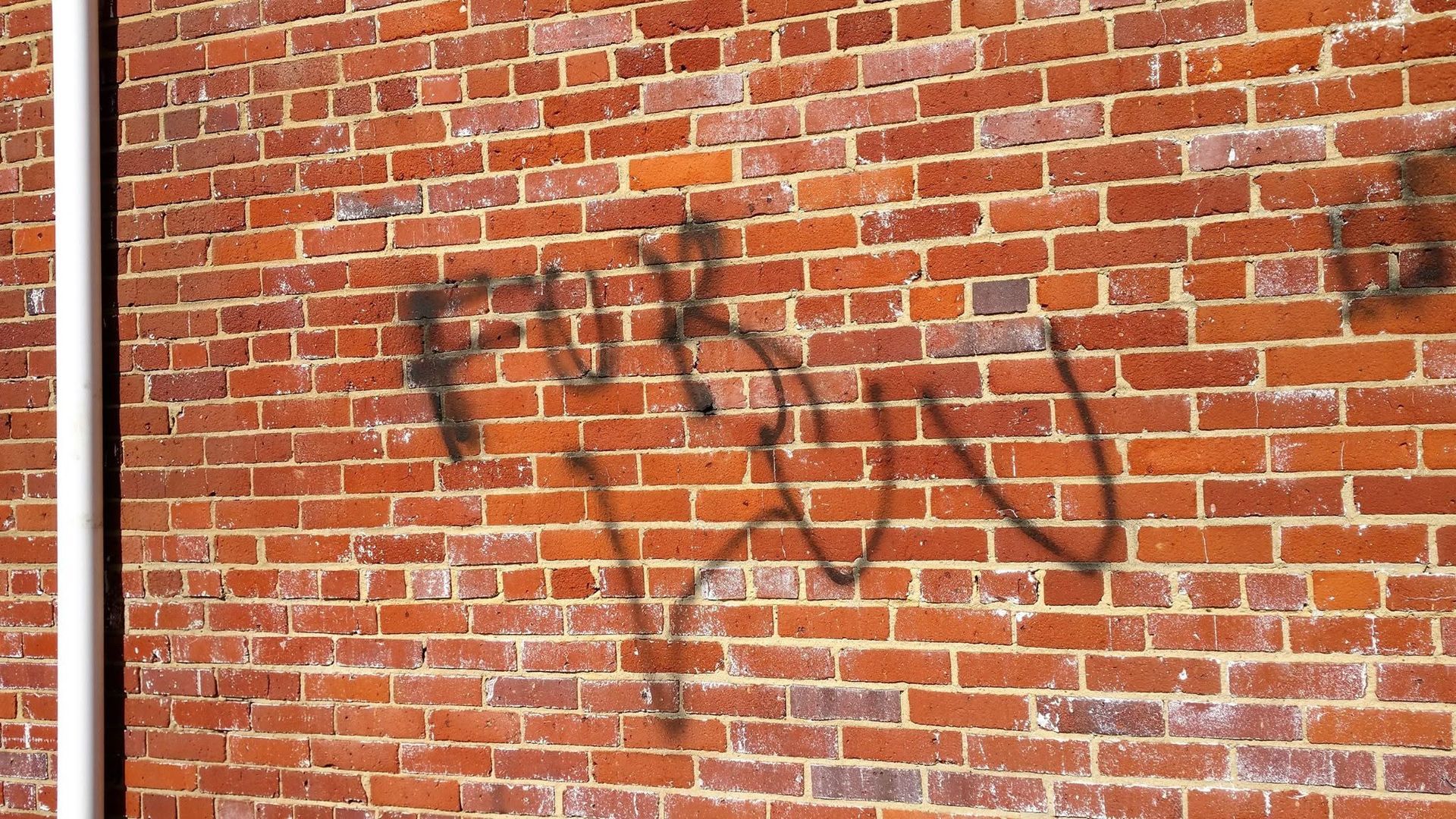 Brick wall with faded black graffiti and weathered red bricks