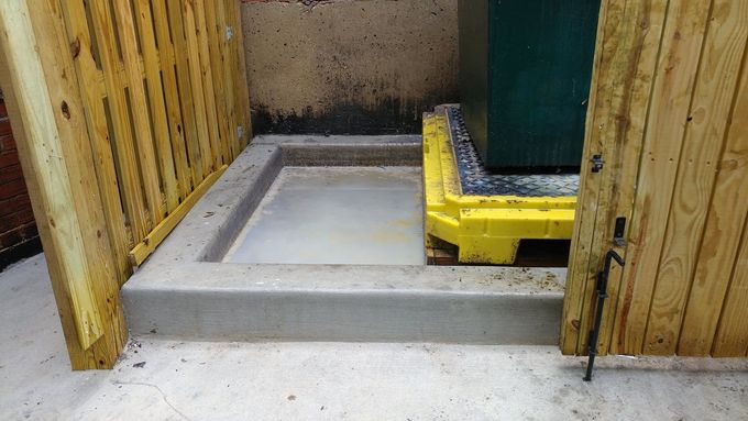 Concrete ramp entrance between wooden fences, with a yellow curb and green door.