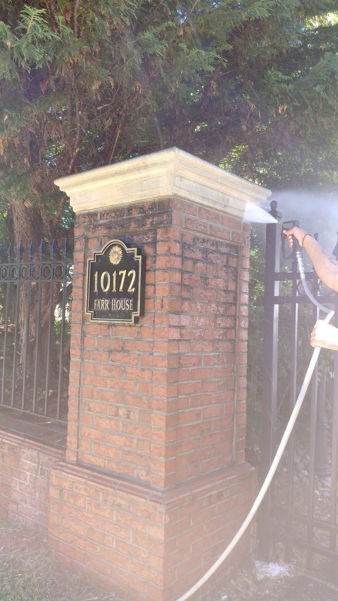 Brick gate pillar with house number plaque being sprayed with water from a hose