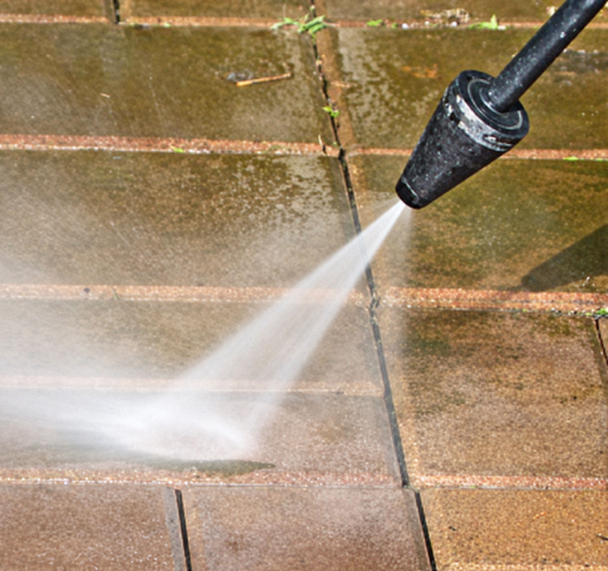 Pressure washer spraying water on a brick patio, cleaning the surface.