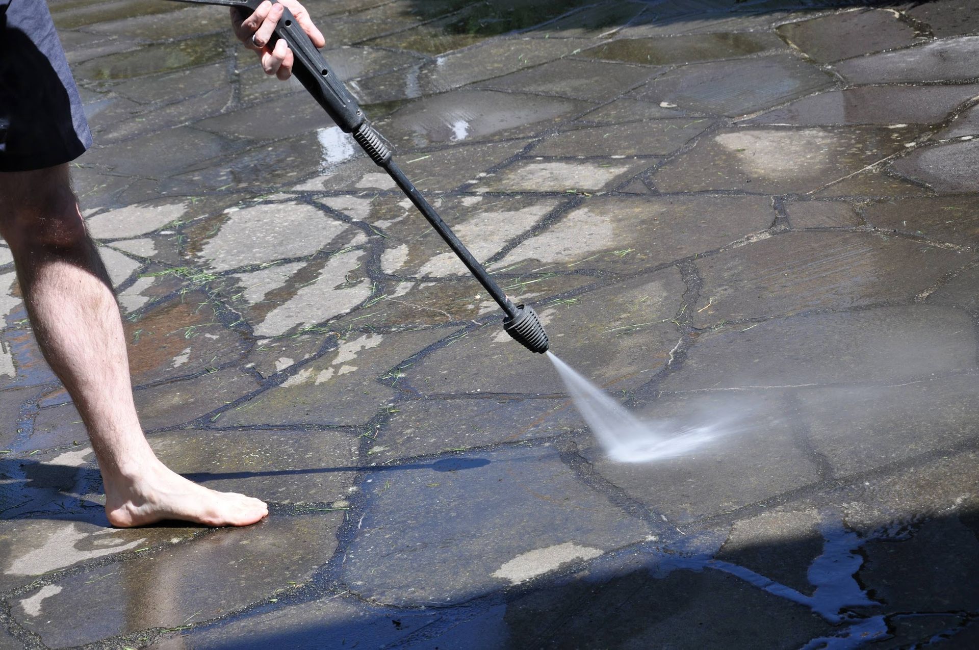Person pressure-washing a wet stone patio with a hose wand