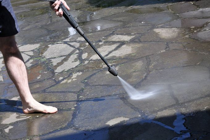 Person pressure-washing a stone patio with a hose, spraying water over wet pavement