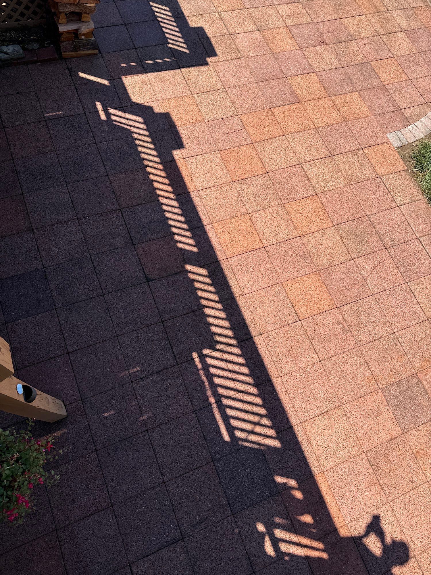 Brick patio with a long diagonal shadow from a railing and a small patch of grass.