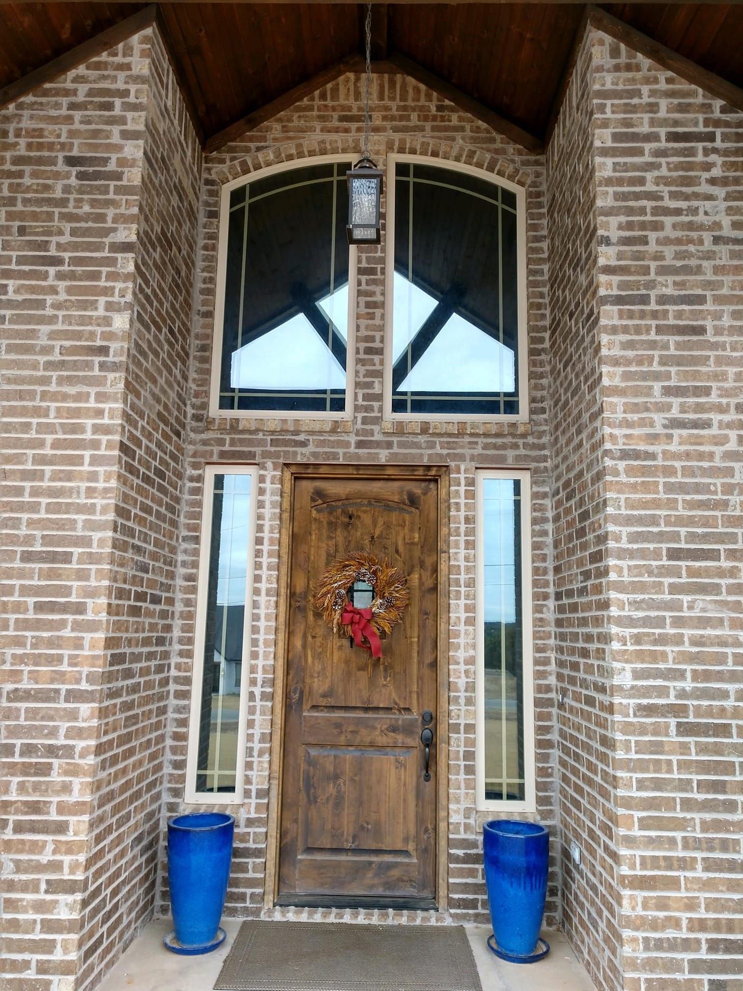 Brick entryway with wooden door, arched windows, and blue planters.