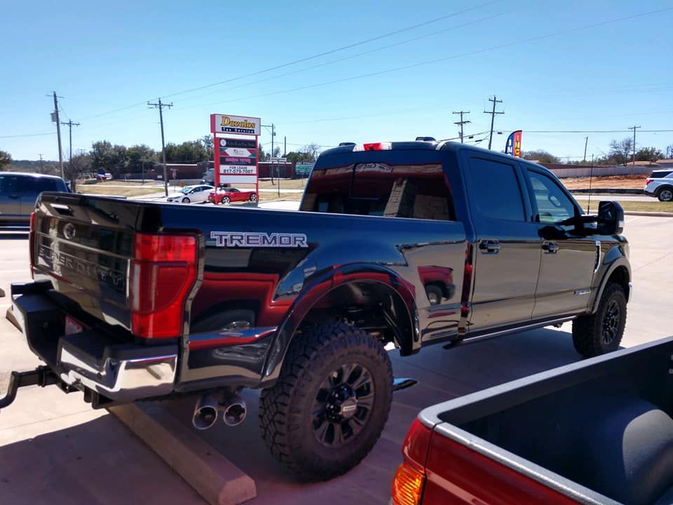 Black Ford F-250 Tremor truck, parked outside on a sunny day. Chrome accents, black wheels, and dual exhaust.