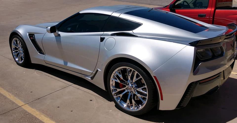 Silver Chevrolet Corvette sports car with chrome wheels parked on pavement.