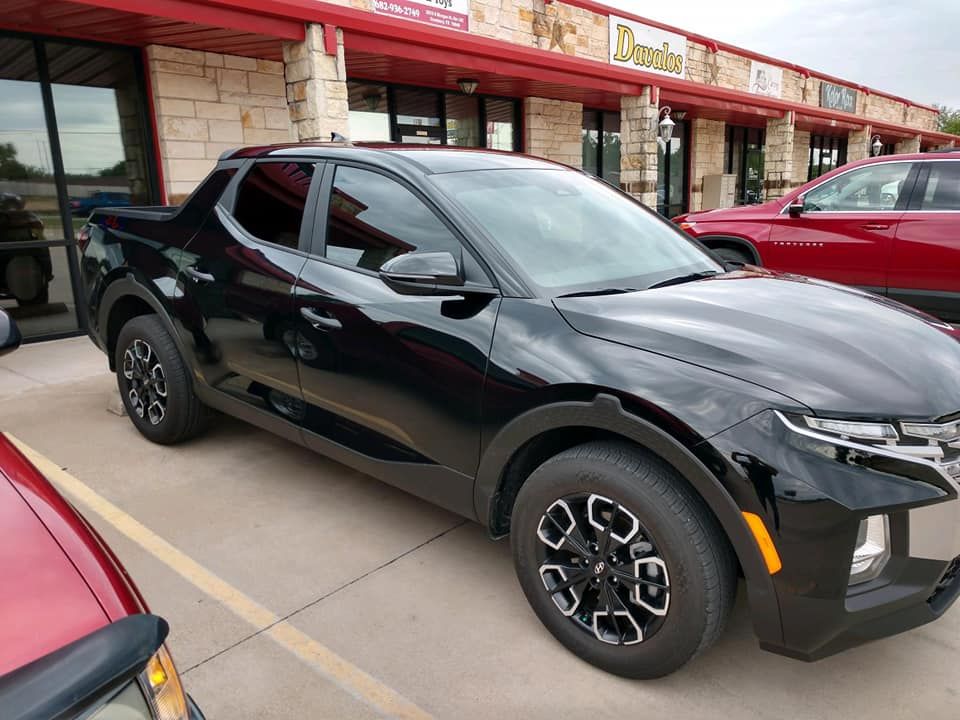 Black Hyundai Santa Cruz pickup truck parked outside a strip mall with a red awning.
