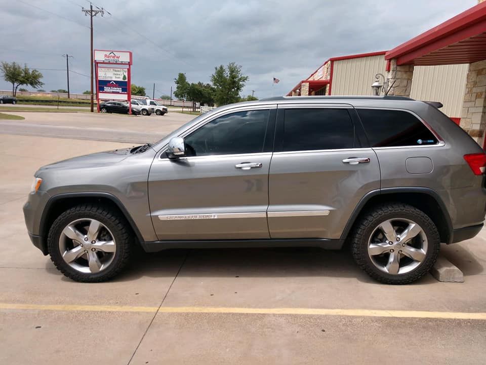 Gray Jeep Grand Cherokee parked in front of a building with tinted windows.
