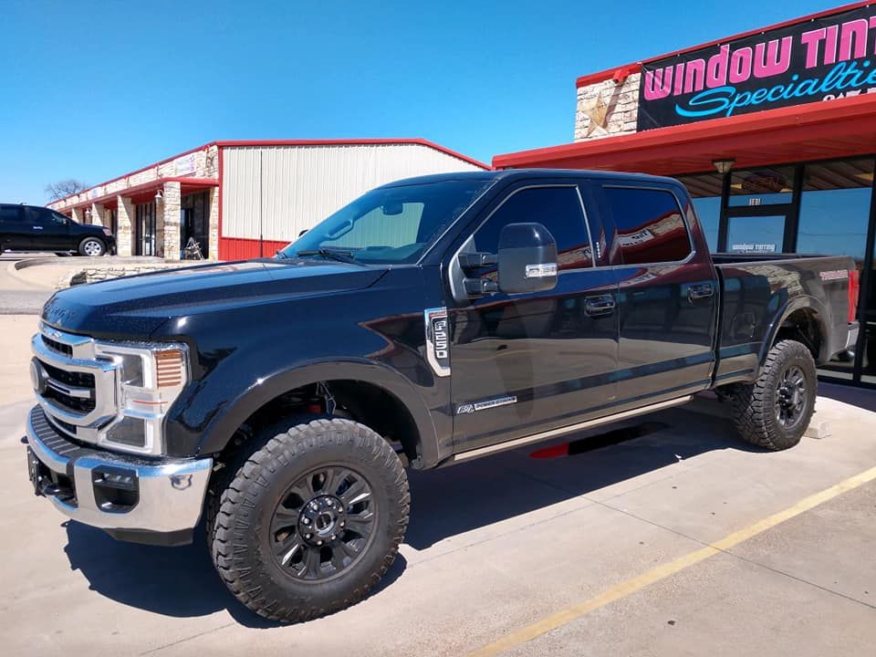 Black Ford pickup truck with tinted windows parked in front of a window tinting business.