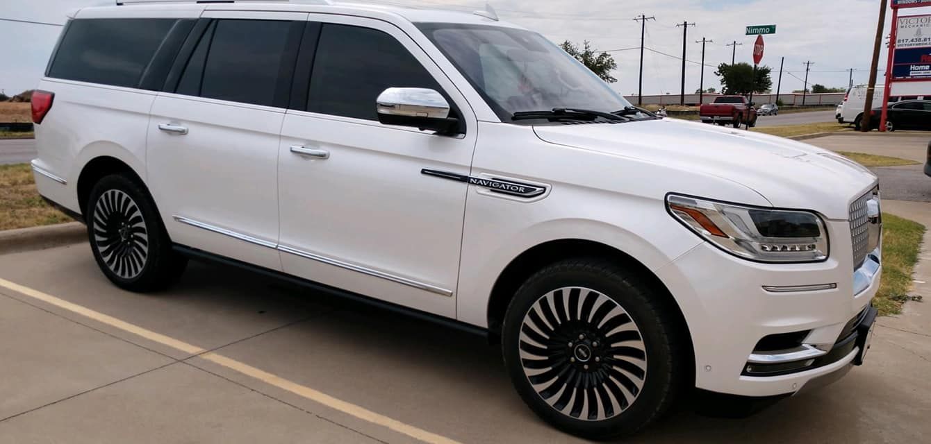 White Lincoln Navigator SUV parked on pavement. Black and silver rims, tinted windows.