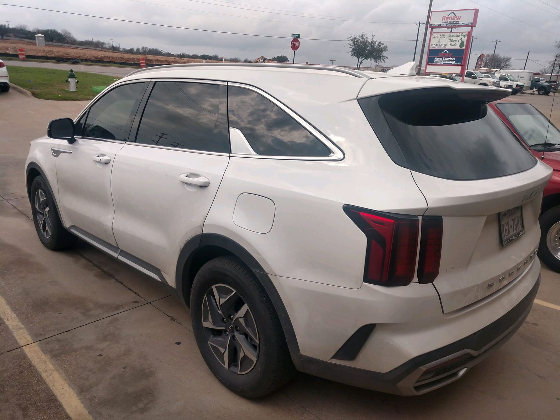 White Kia SUV parked outdoors. Black trim, dark tinted windows, and gray pavement.