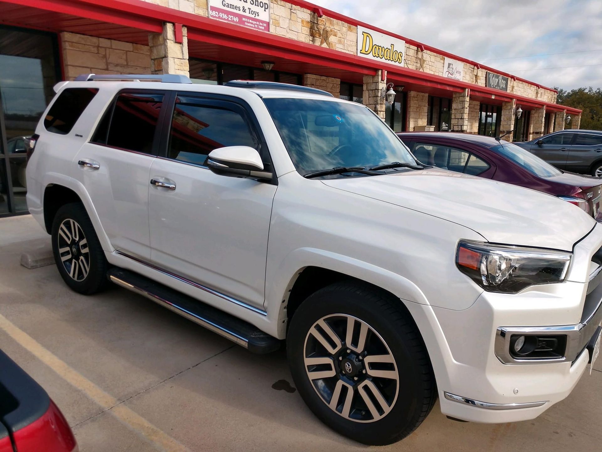 White Toyota 4Runner parked in front of a strip mall with a red awning.