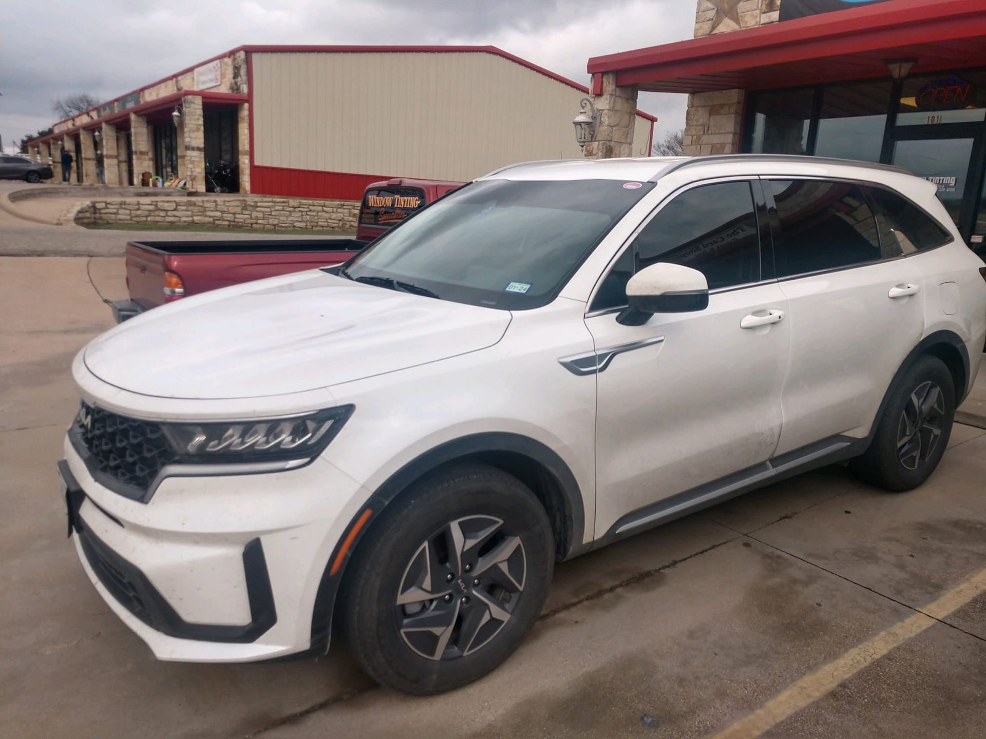 White Kia Sorento SUV parked in front of a building with red awnings. Cloudy sky.