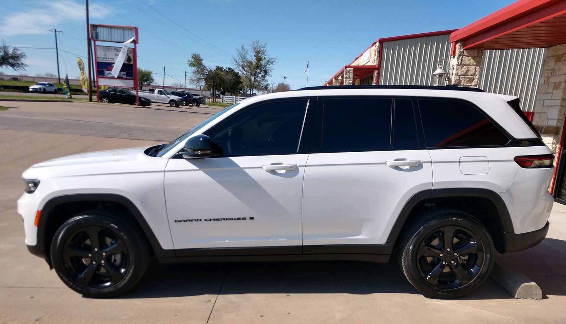 White Jeep Grand Cherokee with black wheels parked outside a business on a sunny day.