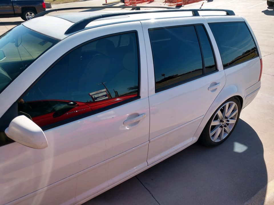 White station wagon with tinted windows parked on concrete. Black roof rack, sunny day.