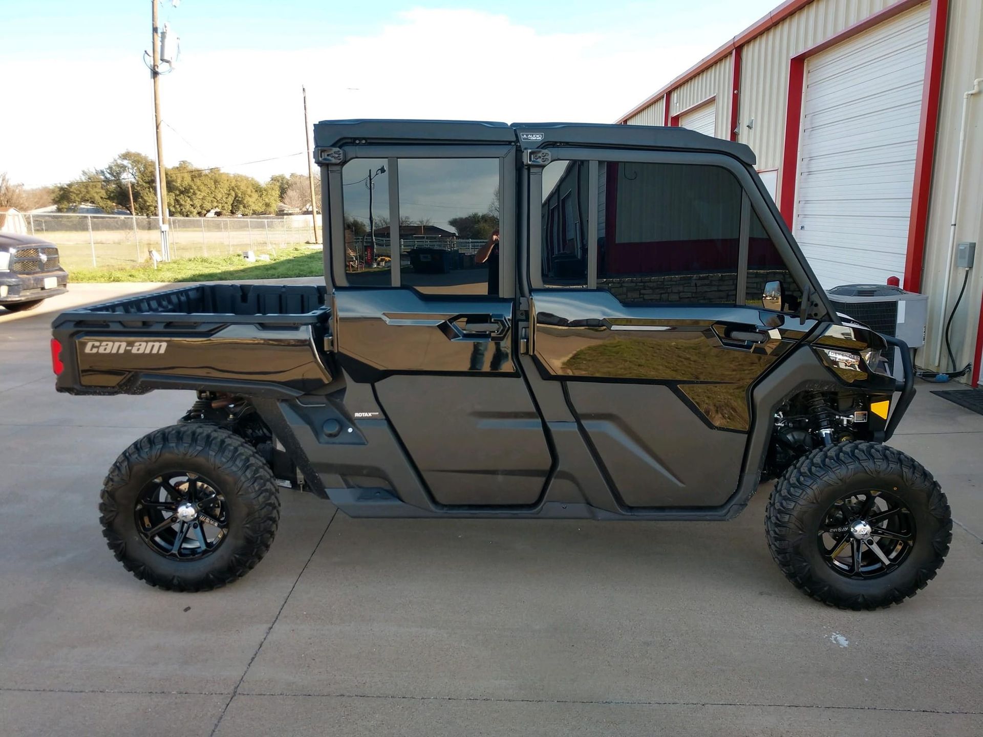 Black Can-Am Defender UTV with black wheels and tinted windows parked in front of a building.