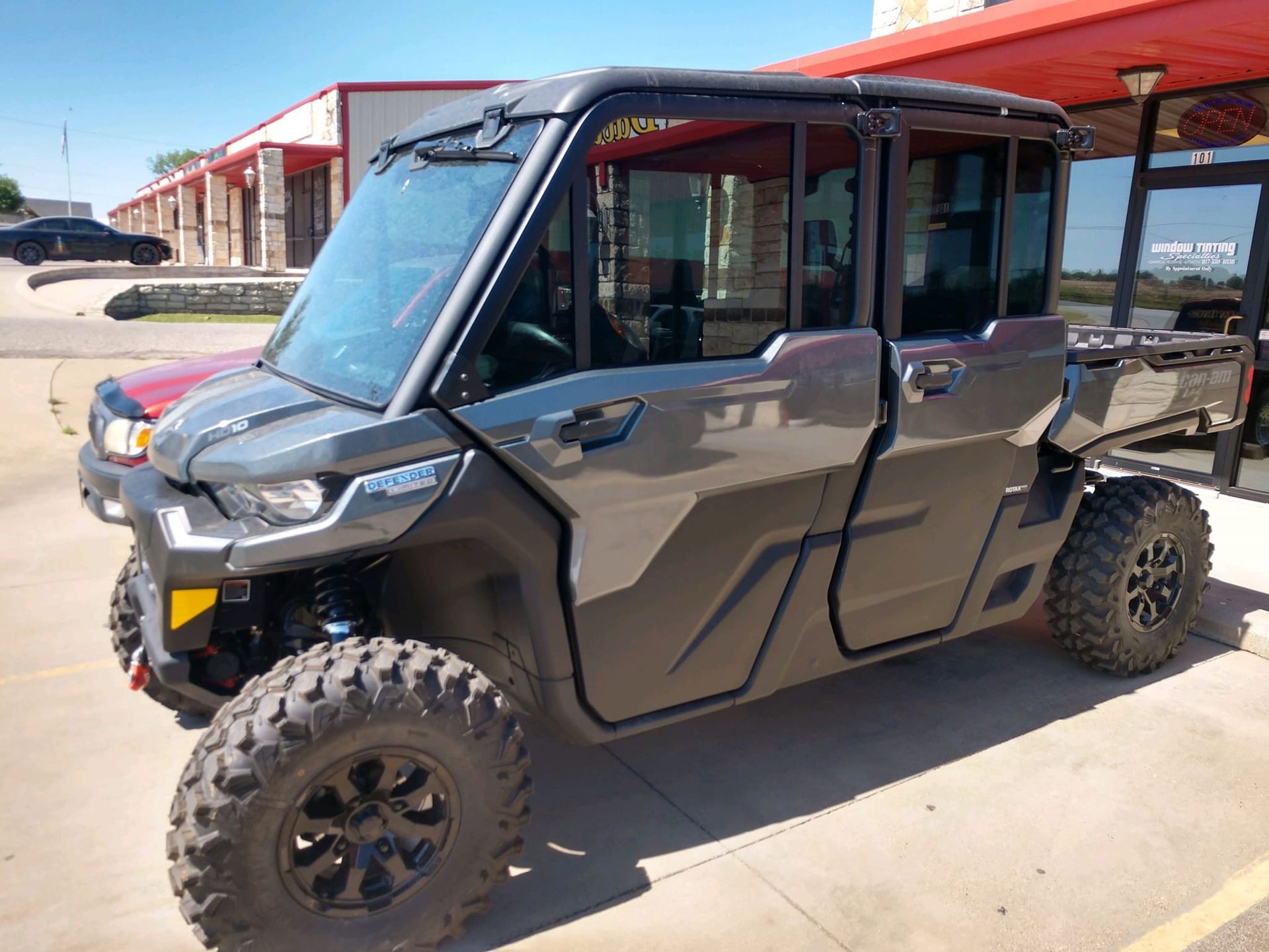 Gray side-by-side UTV with enclosed cabin and large tires parked outside a building.