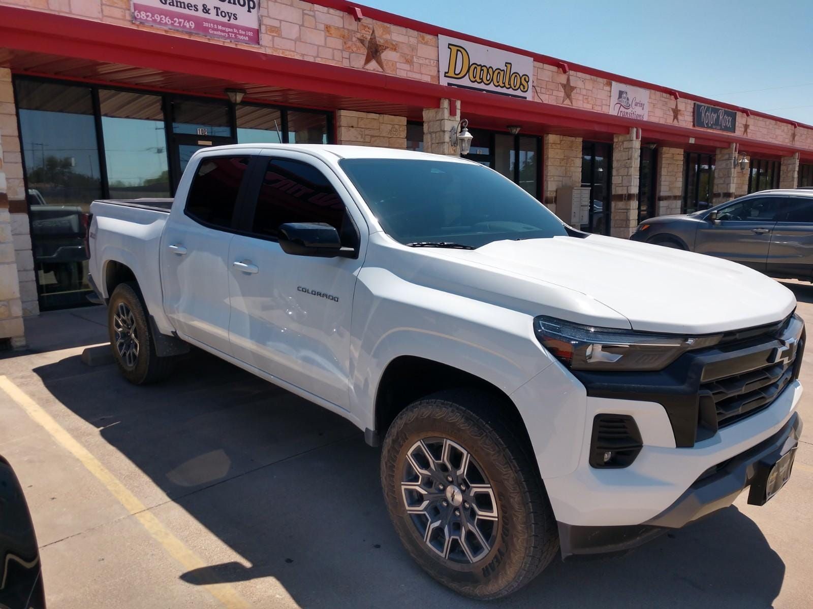 White Chevrolet Colorado truck parked in front of a storefront.