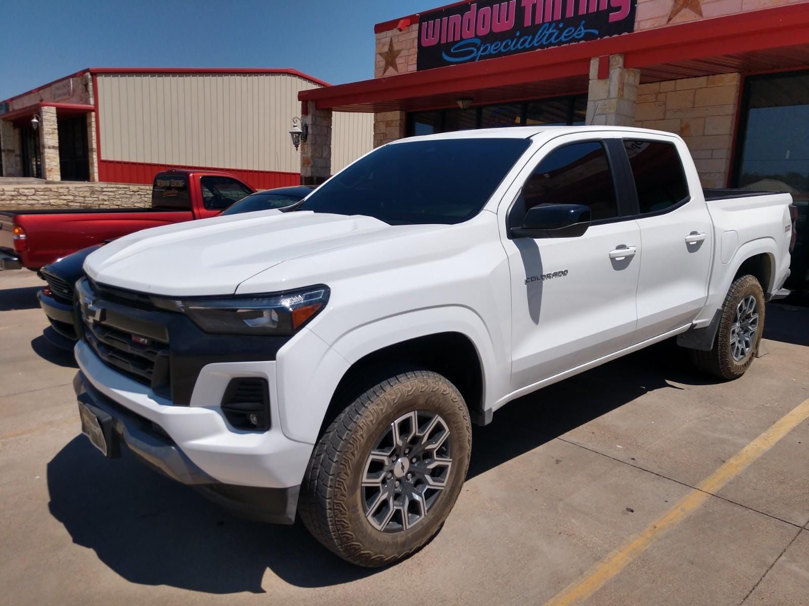 White Chevrolet Colorado pickup truck with tinted windows parked in front of a window tinting business.