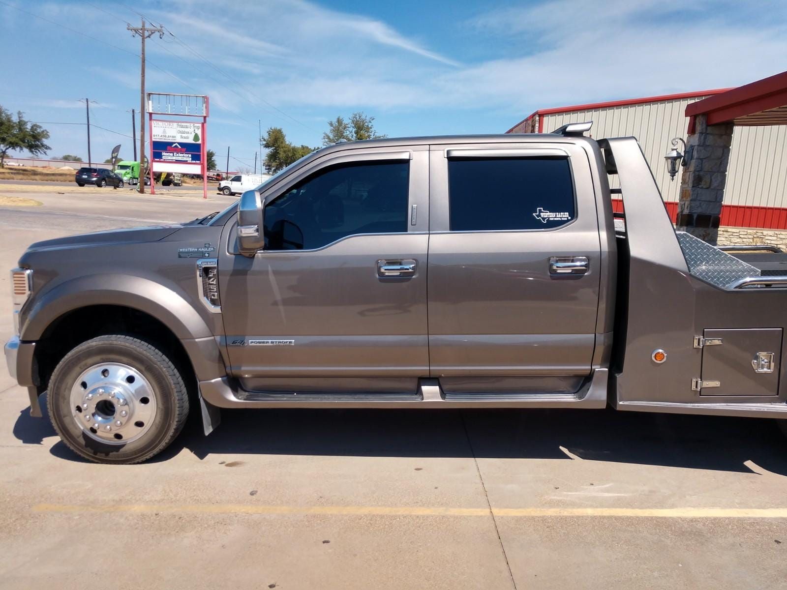 Brown flatbed truck parked outside a building on a sunny day.