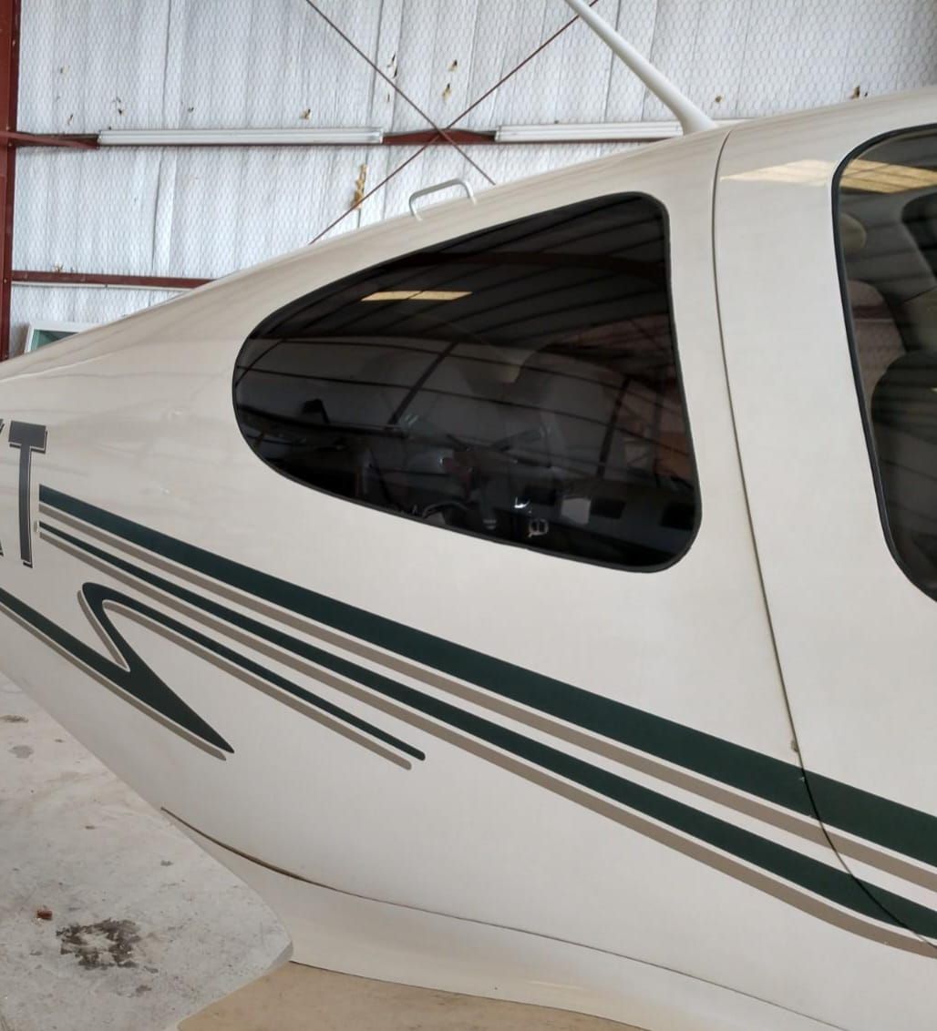 White airplane fuselage with dark green and gray stripes, window showing inside hangar.
