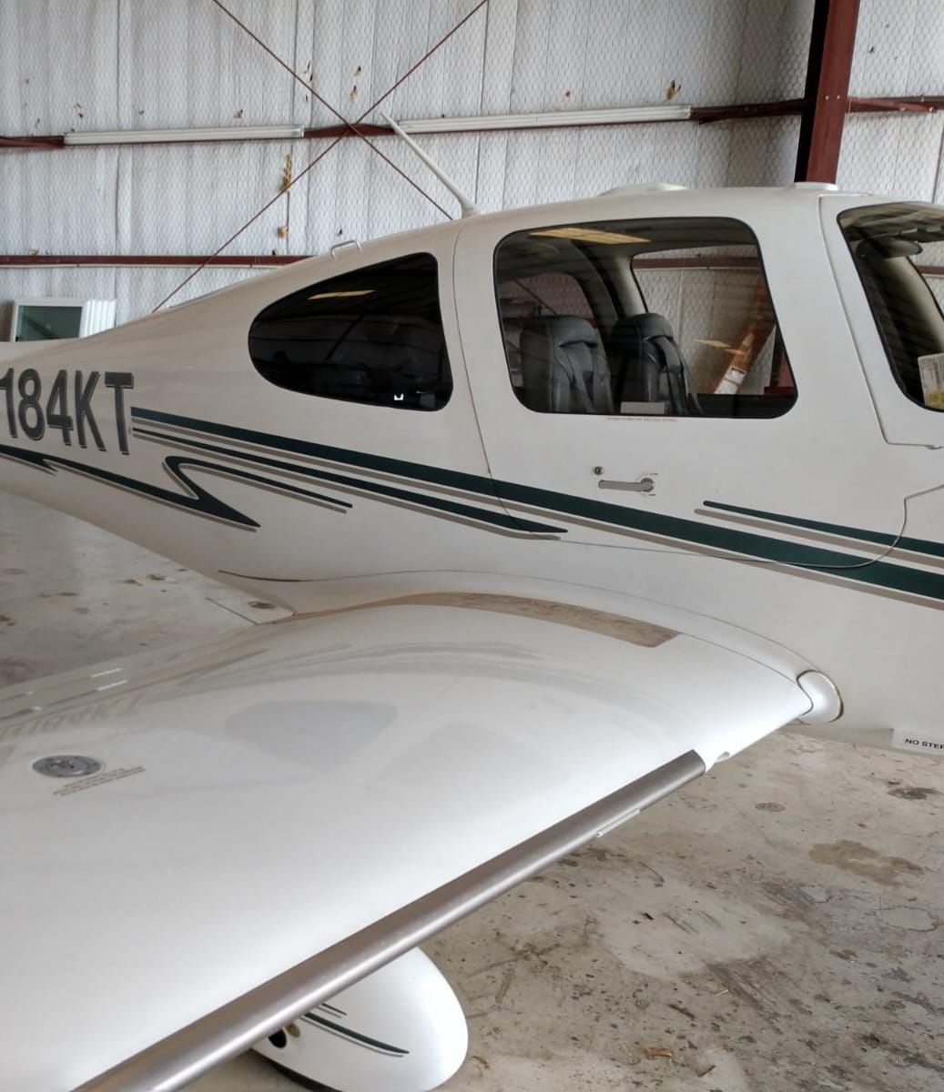 White airplane with green accents parked inside a hangar; visible registration number 