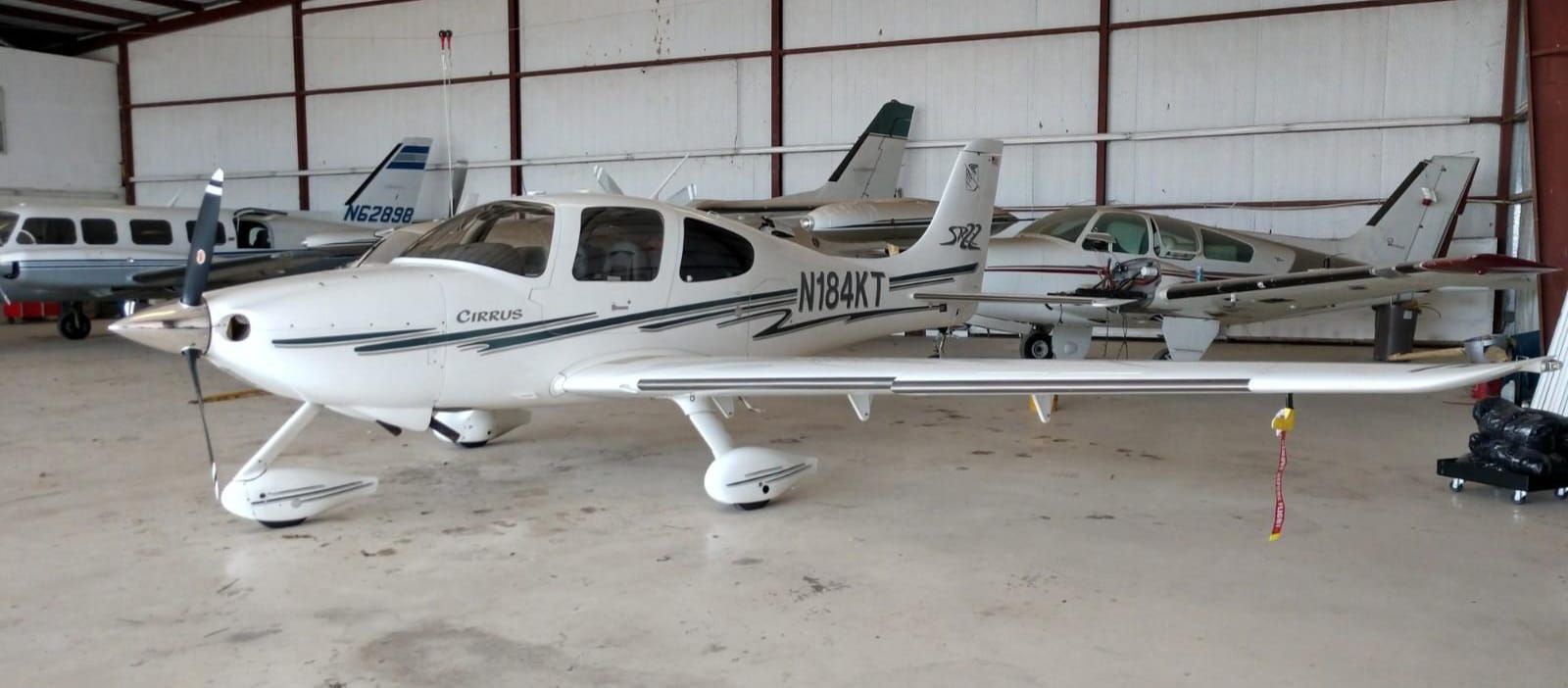 White airplane parked inside a hangar, other planes visible in the background.