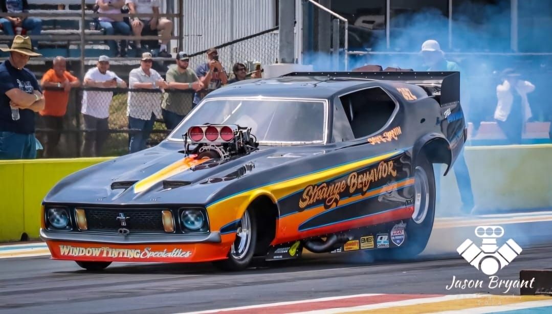 Drag racing car, black and orange flames, smoke, track, crowd.