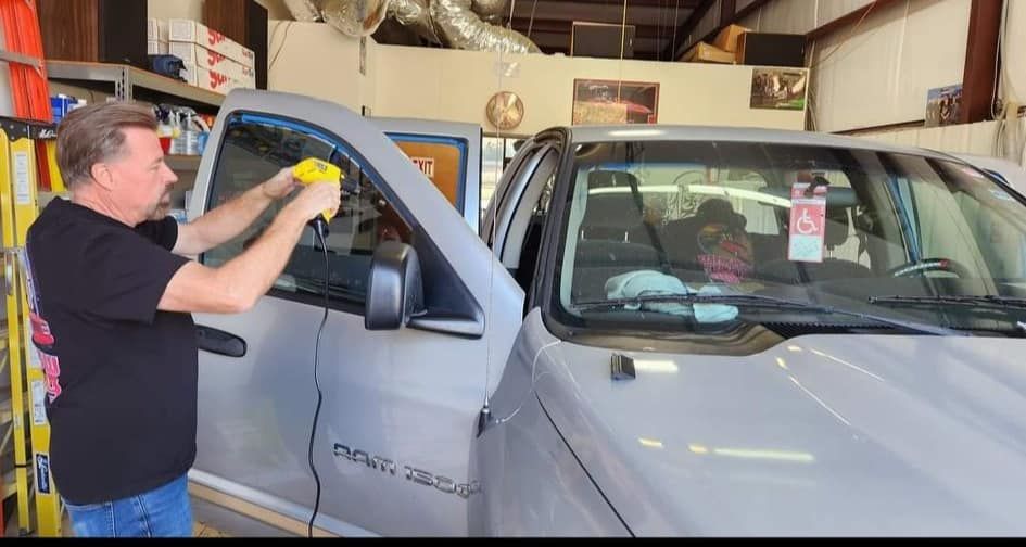 Man cleaning a car window in a garage with yellow cloth. Gray vehicle door is open.