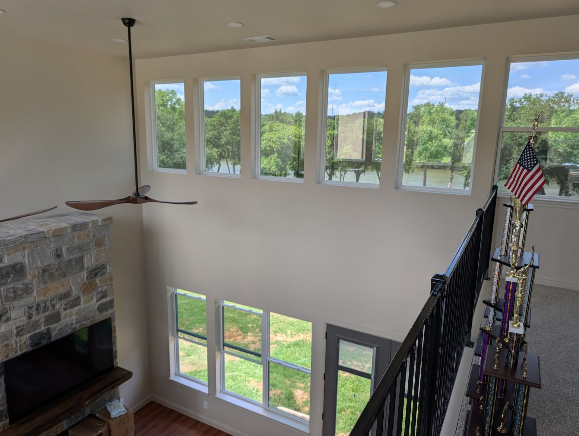 Interior view with tall windows overlooking a lake, a fireplace, and a second-story railing with an American flag.
