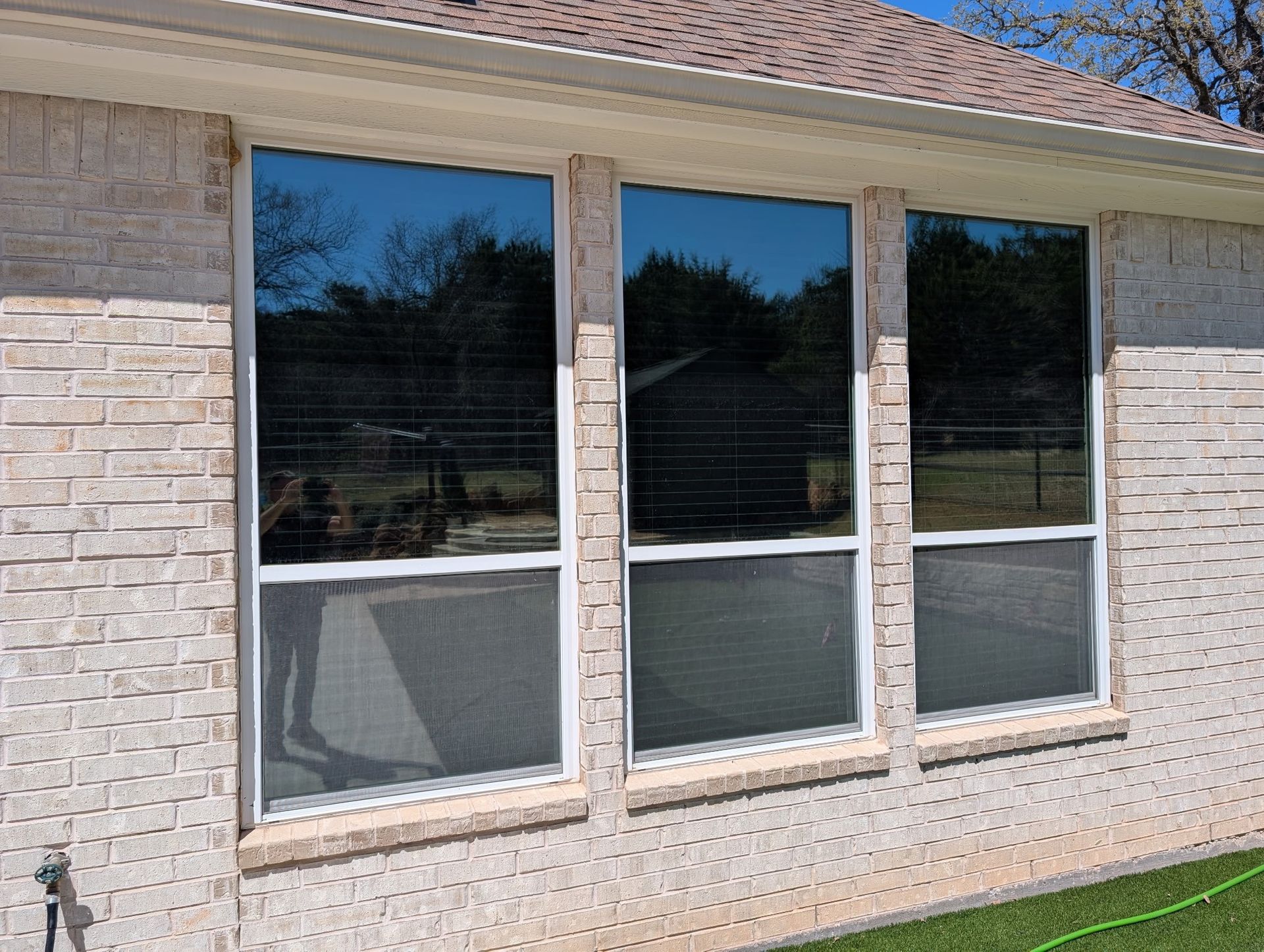 Three rectangular windows with tinted glass on a brick house.