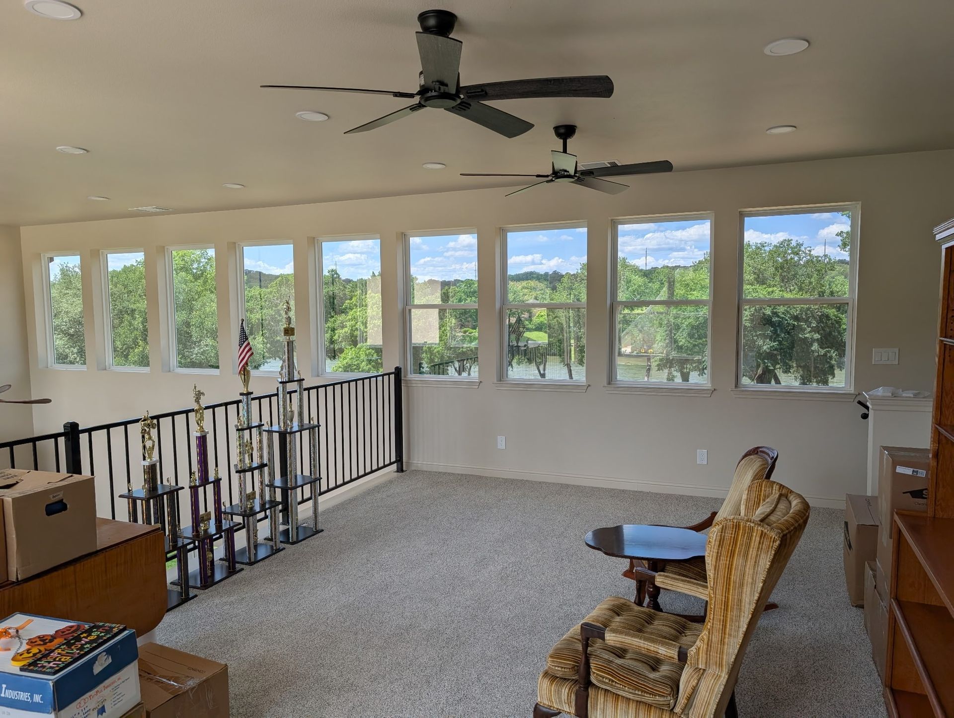 Loft with multiple windows overlooking trees, two ceiling fans, and a carpeted floor.