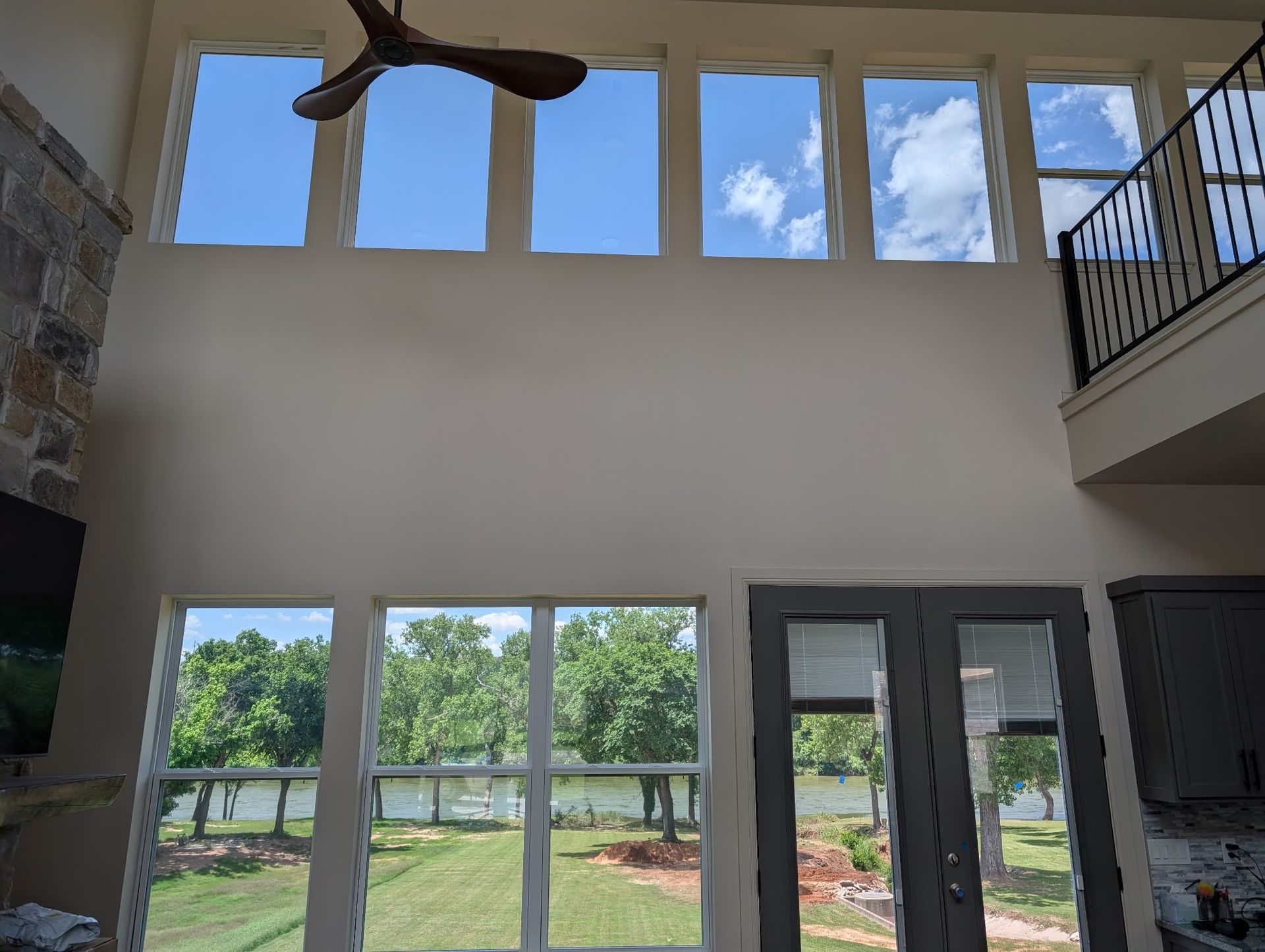 Living room with tall windows overlooking a green yard and water, blue sky, and a balcony.