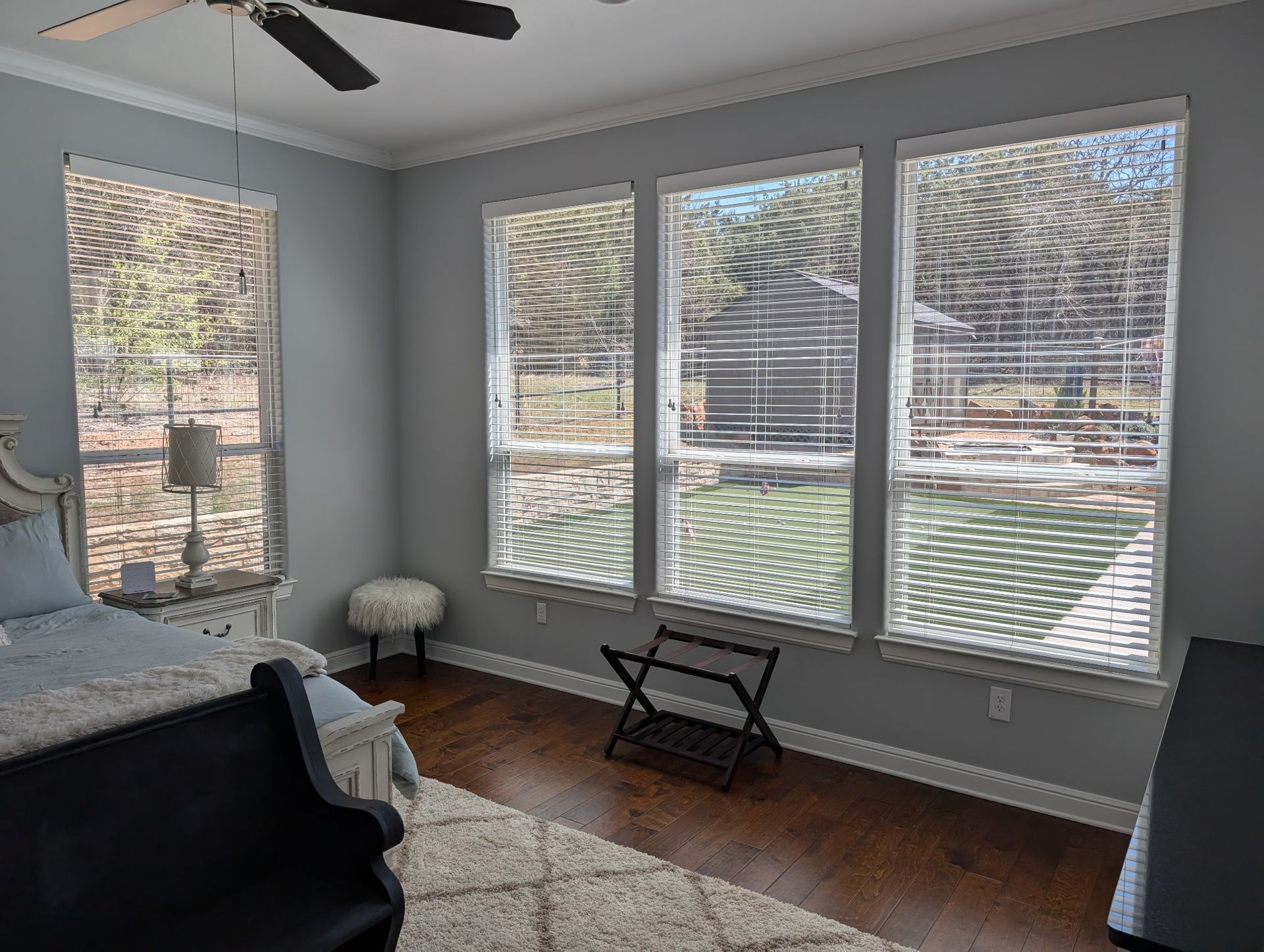 Bedroom with windows and wood floors. Blinds partially cover the windows, showing a yard.