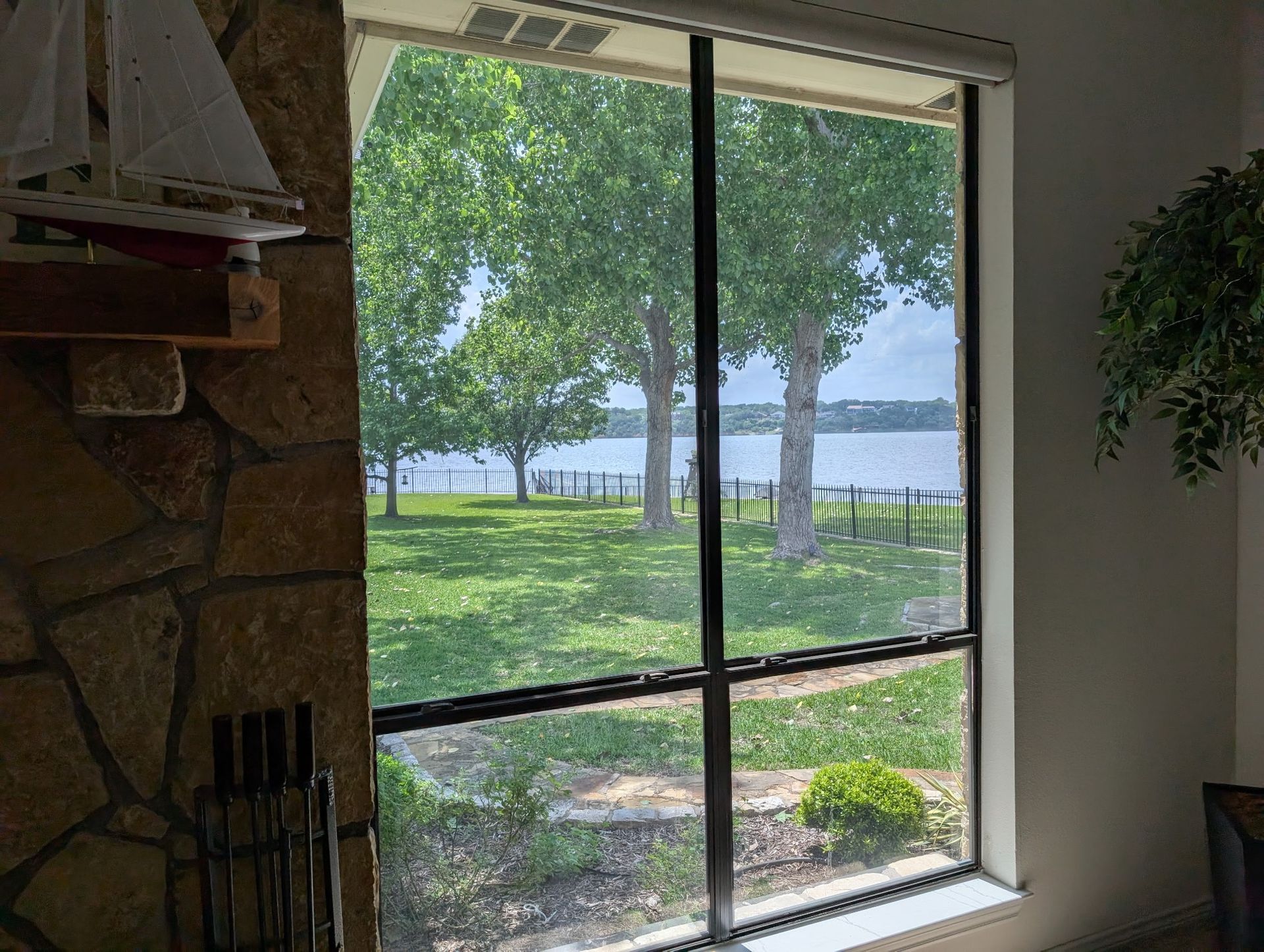 Window view of a lake and green trees, from inside a room with a stone wall and small boat decor.