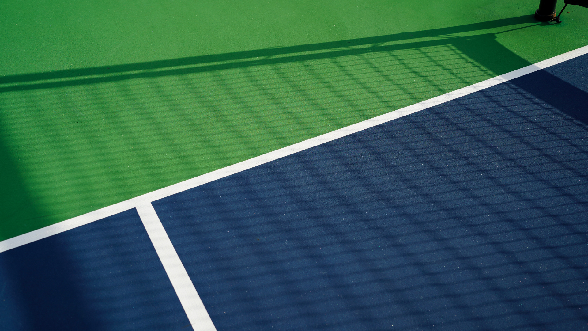 Green and blue sports court with white boundary lines and a diagonal divider