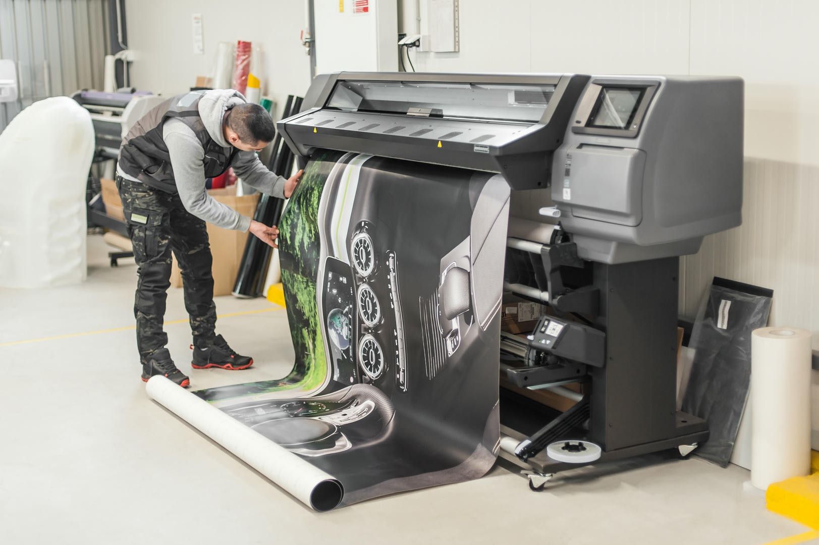 Man examines a large printed graphic rolling out of a wide-format printer in a print shop.