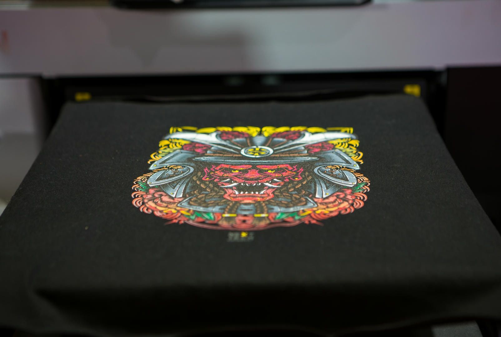 A colorful samurai graphic printed on a black t-shirt during a direct-to-garment printing process.