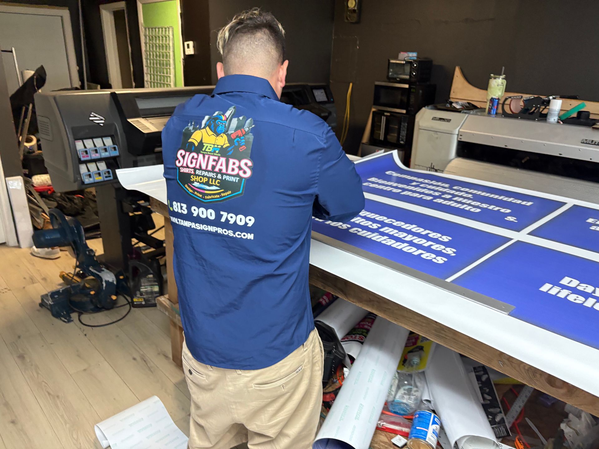 Person applying camouflage car wrap to a vehicle's hood. Green, brown, and tan pattern.