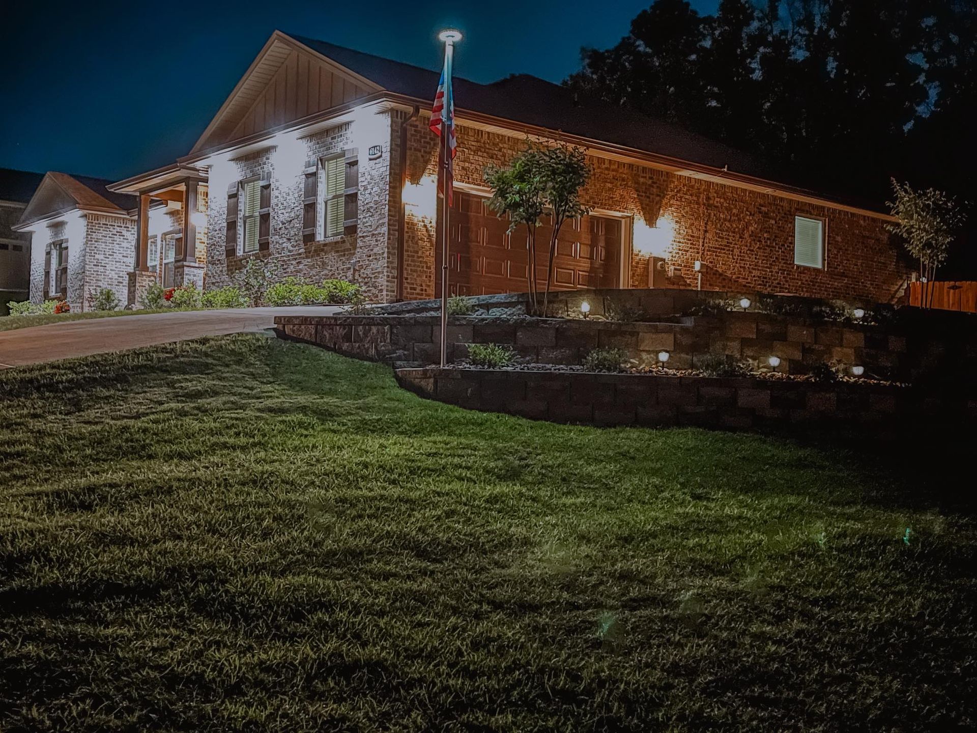 Stone building lit by warm string lights at night beside a grassy slope and stone wall Stone building lit by warm string lights at night beside a grassy slope and stone wall