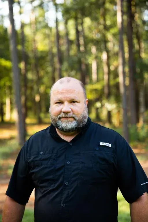 Man in a black shirt standing outdoors in a sunlit forest