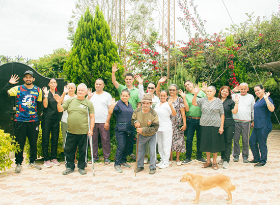 Grupo de personas posando en un jardín, saludando y sonriendo, con un perrito en primer plano.