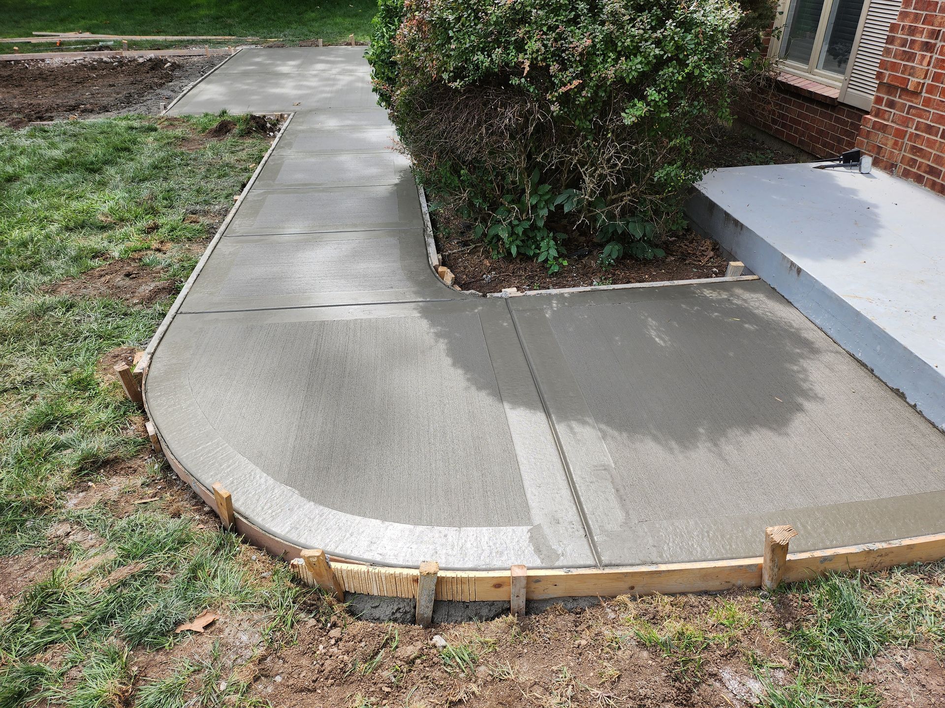 A concrete walkway is being built in front of a brick house.