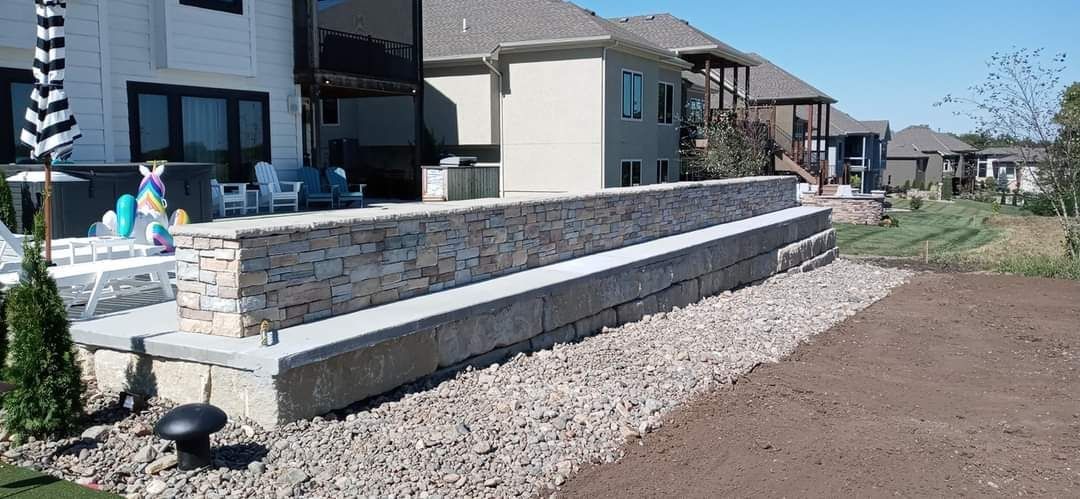 A stone wall surrounds a gravel driveway in front of a house.